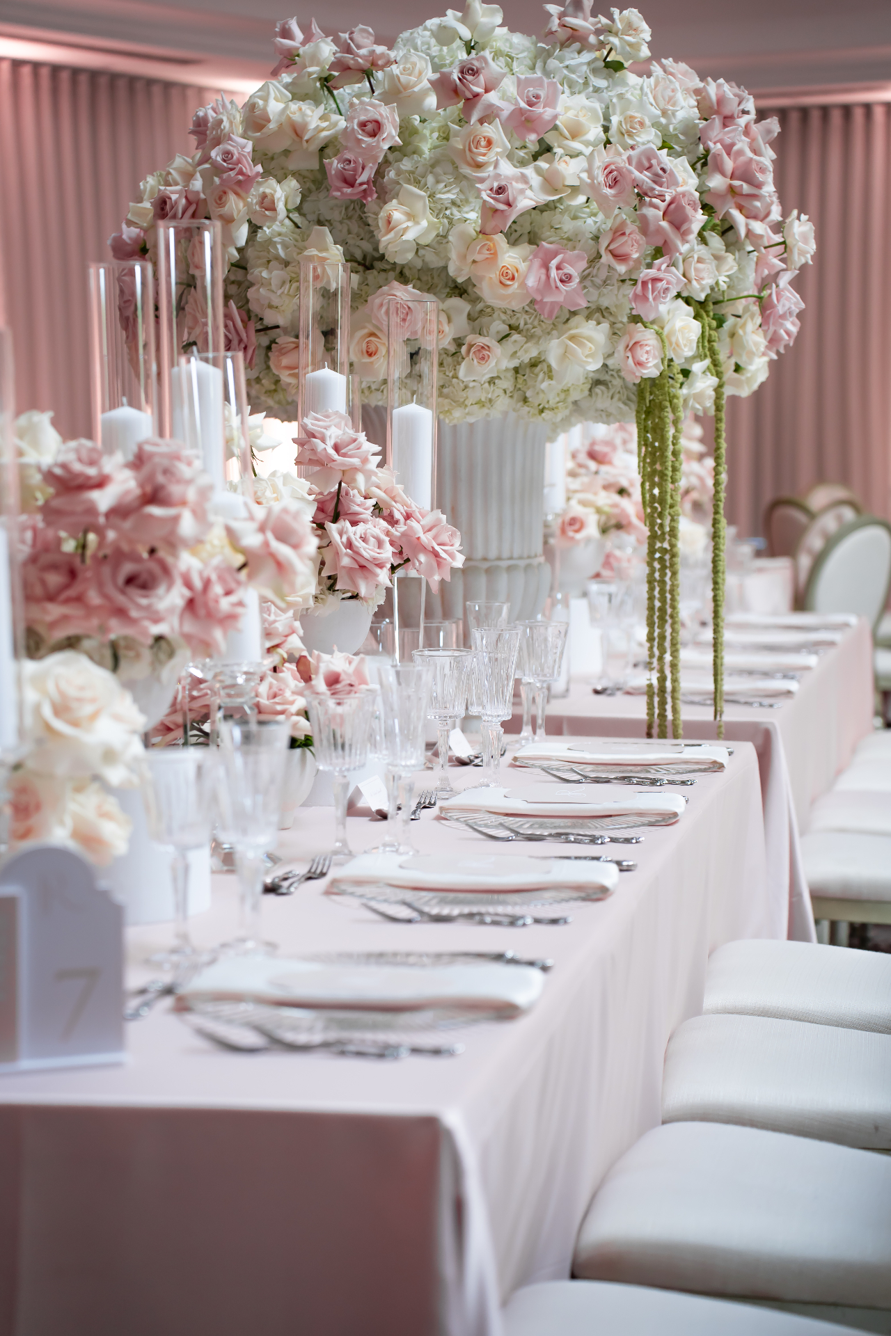 Blush Rose Tall Centerpiece - Towering blush rose and white hydrangea centerpiece with cascading green amaranthus and pillar candles along a long blush reception table by Aura Floral Design Miami