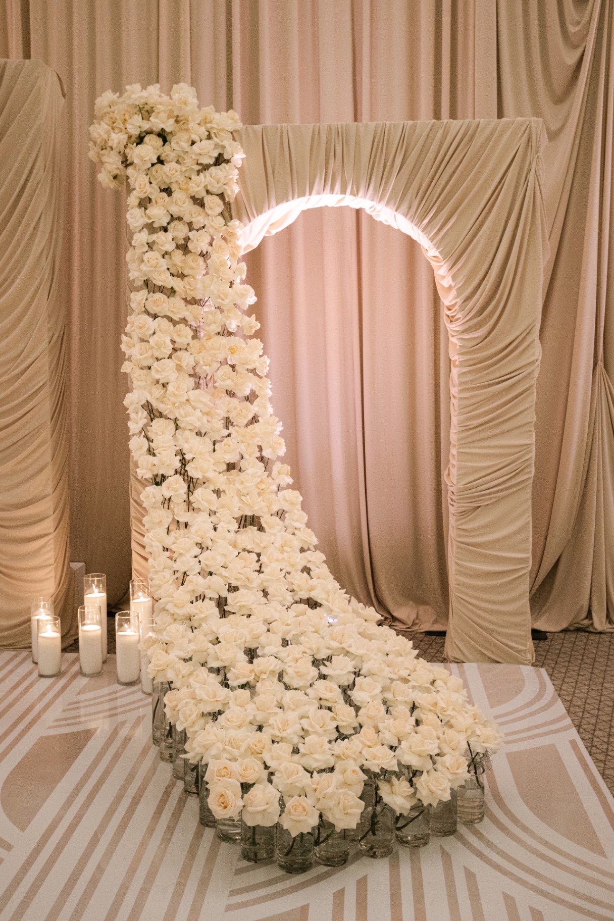 Cascading White Rose Arch - Towering cascade of ivory roses spilling from a champagne draped arch with pillar candles by Aura Floral Design Miami