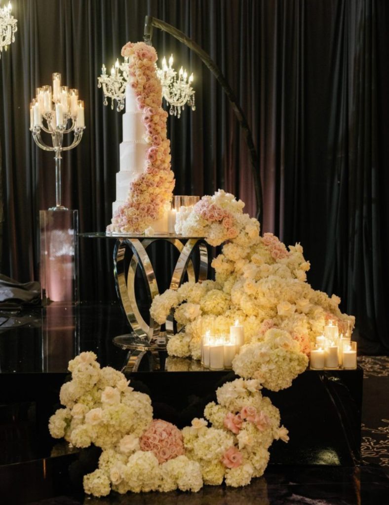 Cascading Cake Florals - Tiered wedding cake adorned with roses and lush floral cascade by Aura Floral Design Miami